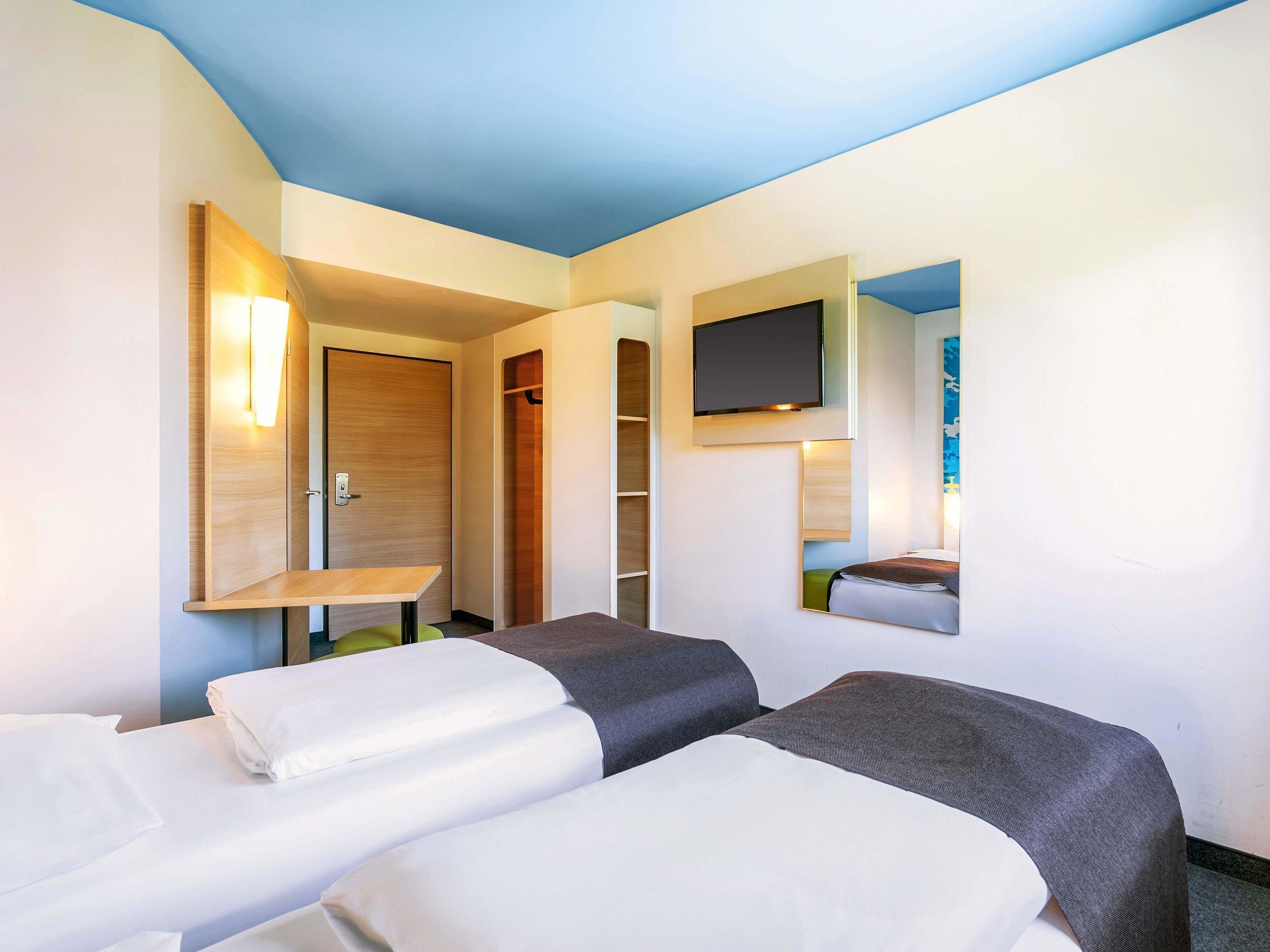 Habitación de hotel con dos camas, un televisor montado en la pared y una puerta de madera.