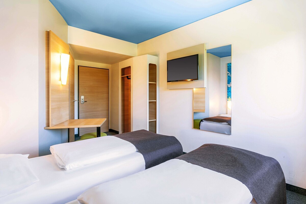 A hotel room with two beds, a TV mounted on the wall, and a wooden door.