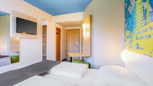 A hotel room with a bed, a desk, a chair, a TV mounted on the wall, and a closet. - B&B Hotel Stuttgart-City (Stuttgart)
