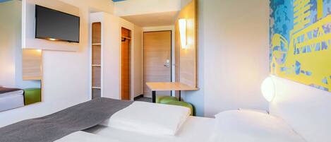 A hotel room with a bed, a desk, a chair, a TV mounted on the wall, and a closet.