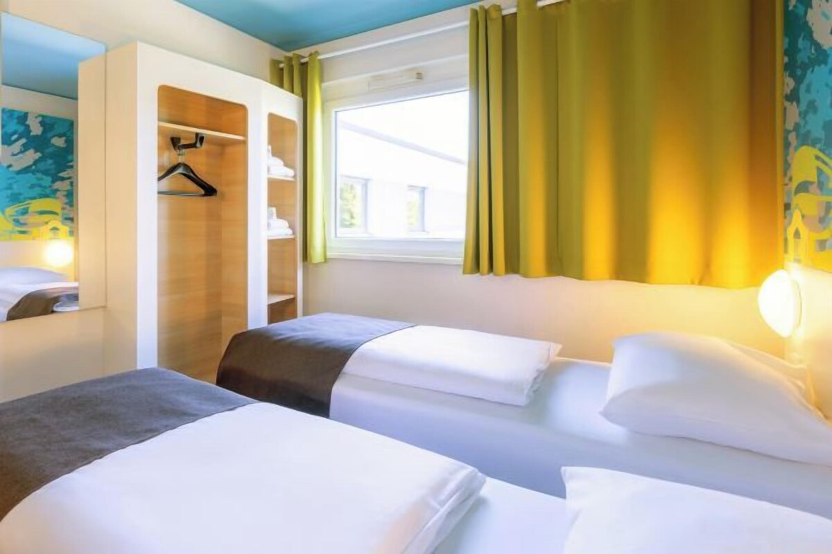 Habitación de hotel con dos camas, un armario y una ventana con cortinas.
