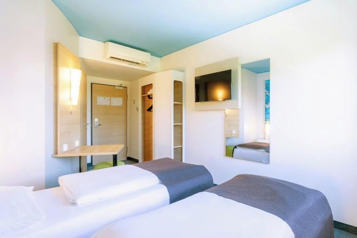Habitación de hotel con dos camas, un espejo, un armario y un pequeño rincón de descanso.