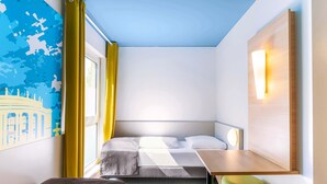 A compact hotel room with a bed, a small desk, a chair, and a wall-mounted light fixture. - B&B Hotel Stuttgart-City (Stuttgart)