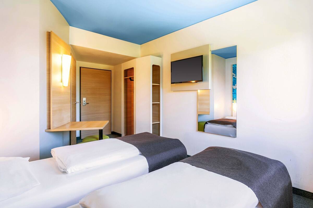 Habitación de hotel con dos camas, un televisor montado en la pared y una puerta de madera.