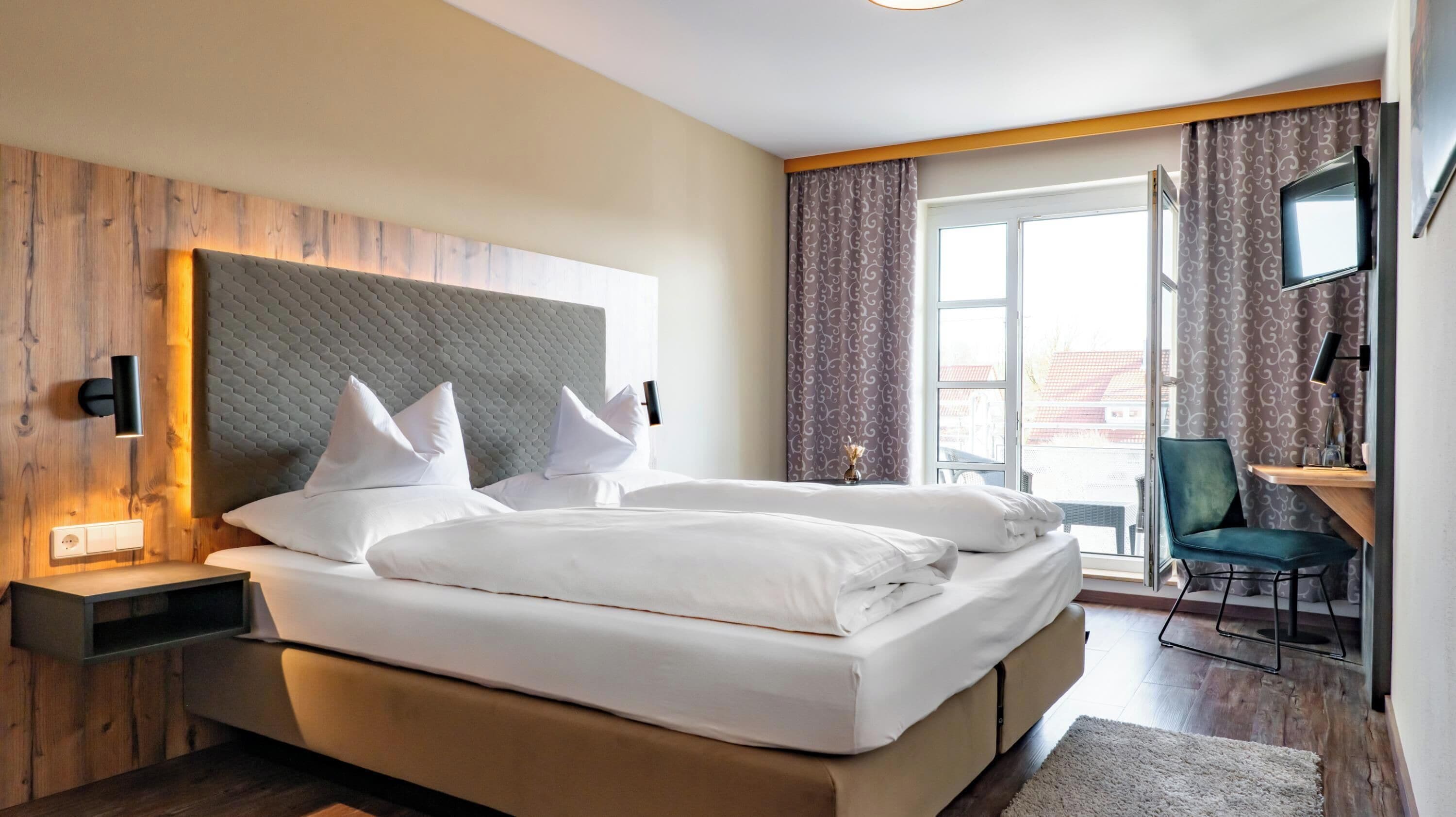 A hotel room with a large bed, a desk with a chair, a television, and a window with curtains.