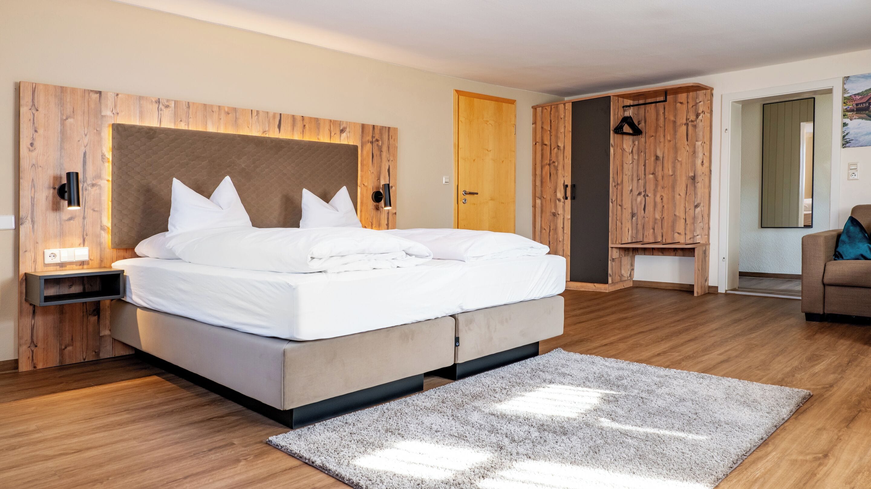 Een moderne slaapkamer met een groot bed, een houten hoofdbord, nachtkastjes, een garderobe en een spiegel.