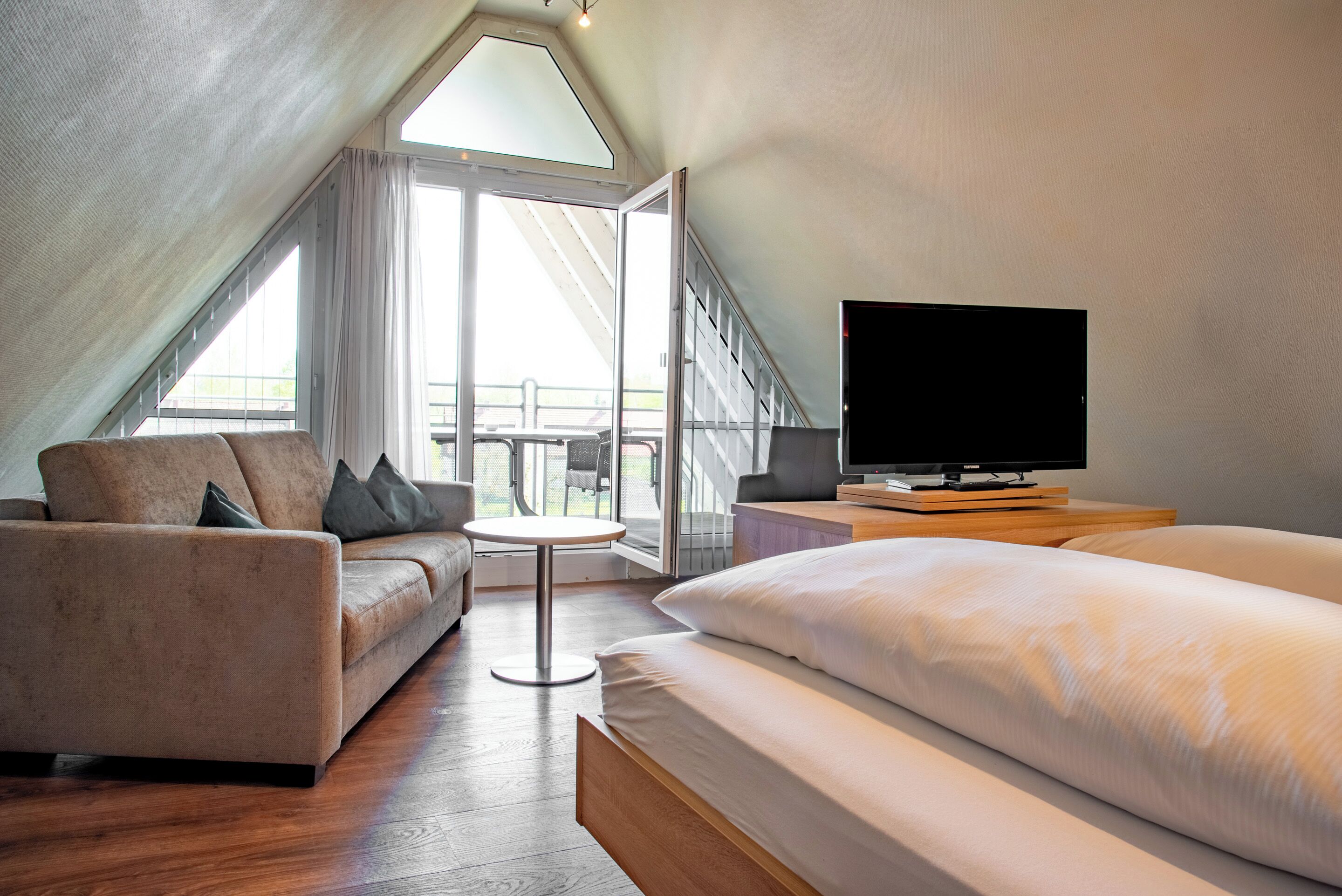 A modern bedroom with a bed, a sofa, a TV, and a balcony with a view.