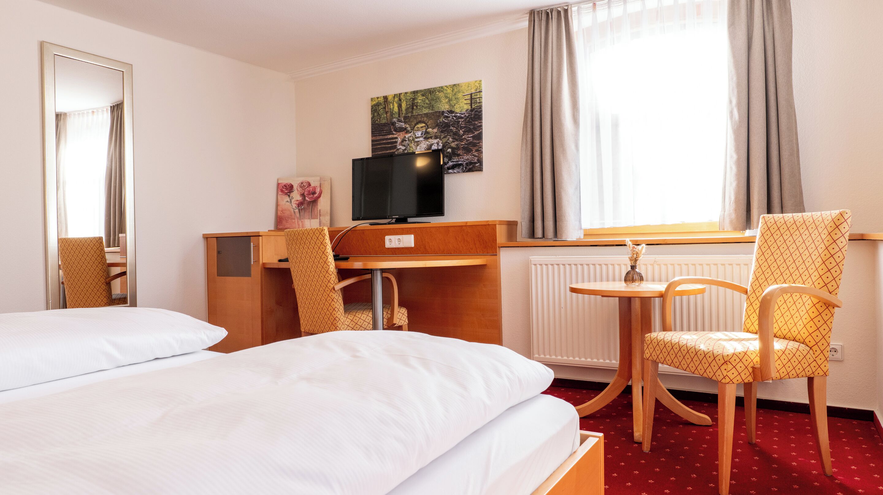 A hotel room with two beds, a desk with a television, a chair, and a window with curtains.