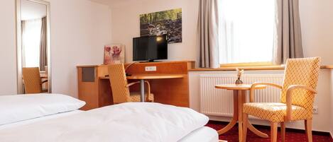 A hotel room with two beds, a desk with a television, a chair, and a window with curtains.
