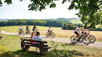 A group of cyclists on a paved path with a bench and greenery in the foreground.