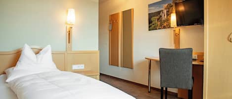 A hotel room with a bed, desk, chair, and a TV mounted on the wall.