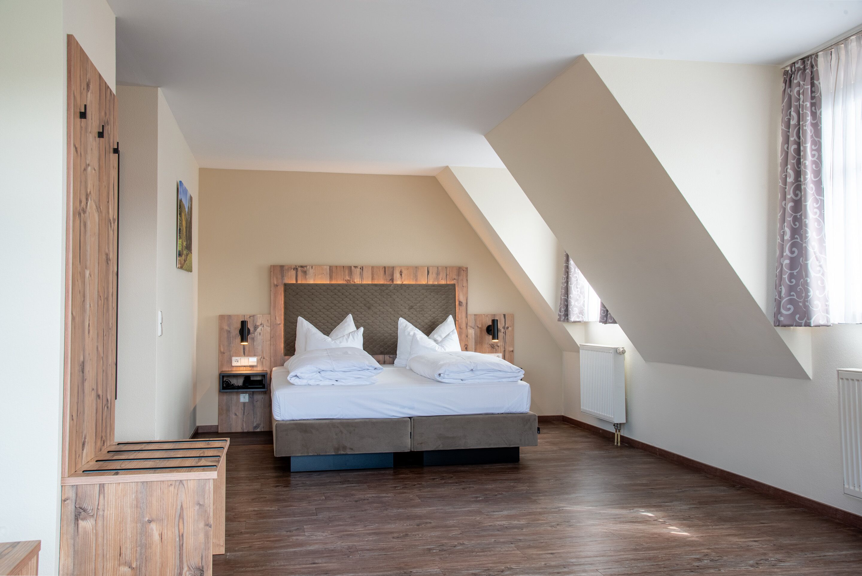 Et soveværelse med en stor seng, træsenggavl og et skråt loft.