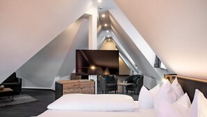 Une chambre moderne aménagée dans les combles, de forme triangulaire, comprenant un lit, un coin salon et un téléviseur à écran plat.