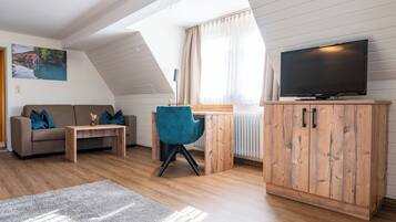 Een gezellige woonkamer met een bank, een blauwe fauteuil, een houten kast en een televisie.