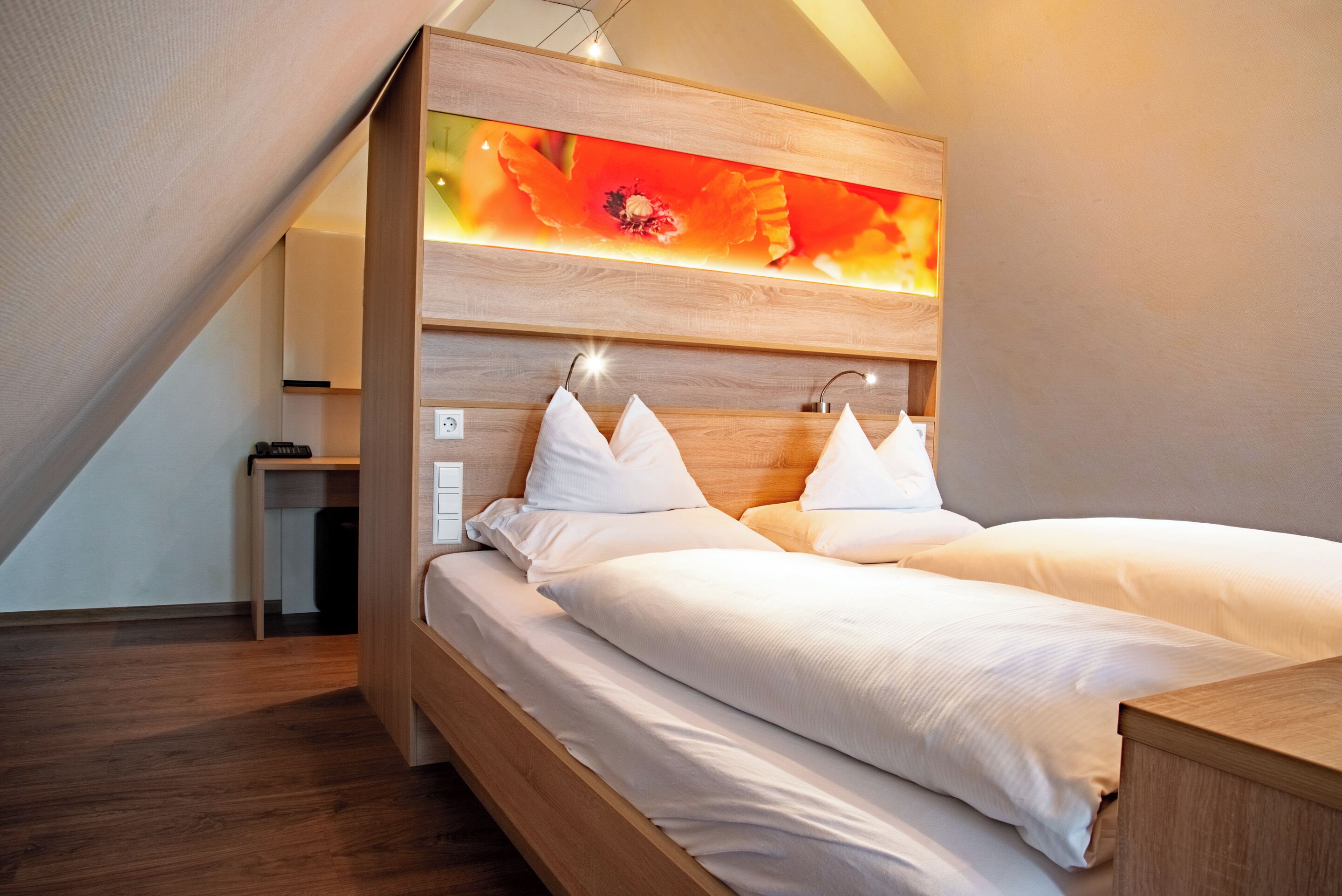 A modern bedroom with a sloped ceiling, a wooden headboard, and a large wall-mounted artwork.