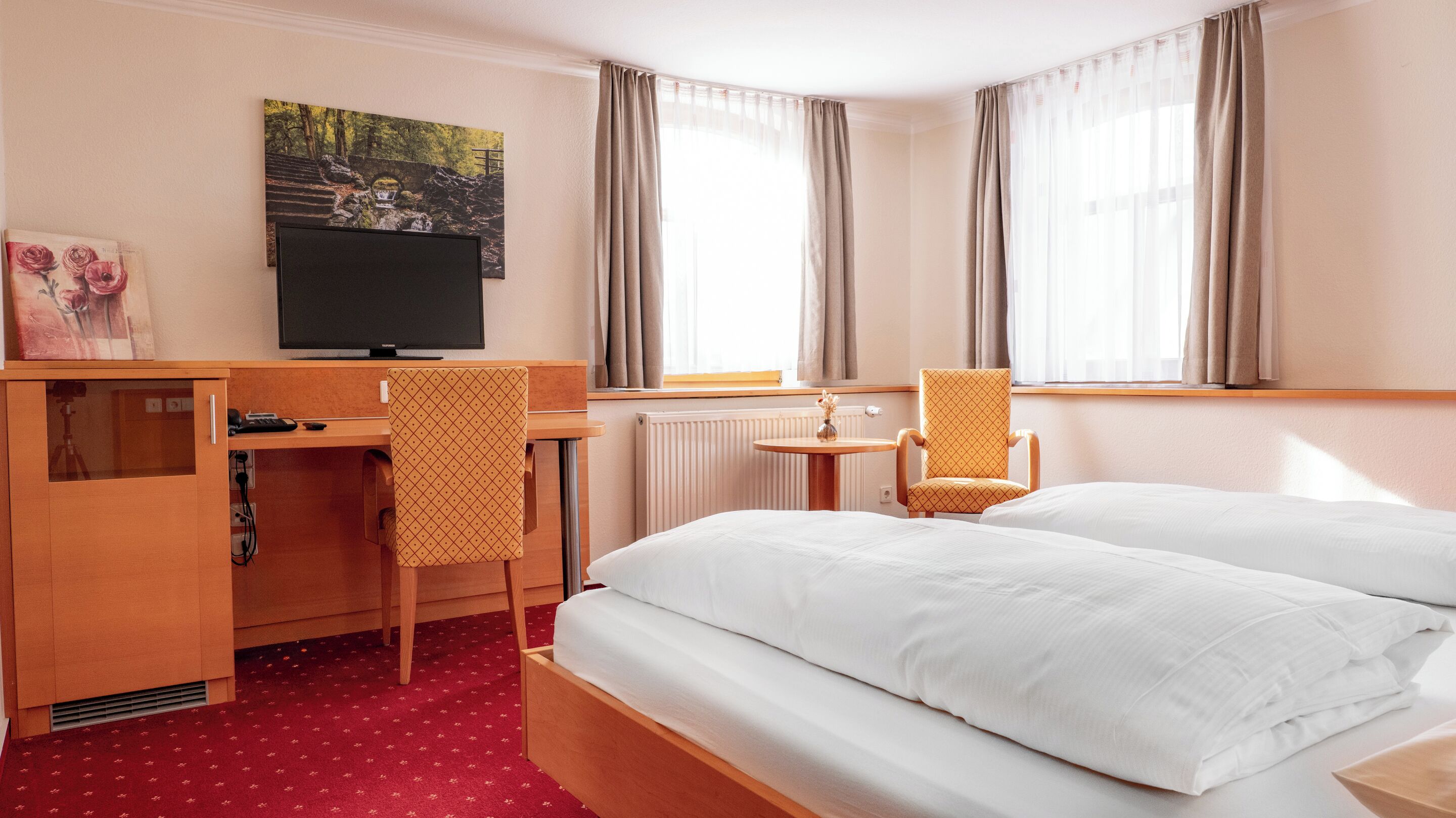 Ein Hotelzimmer mit Bett, Schreibtisch, Stuhl, Fernseher und einem Fenster mit Vorhängen.