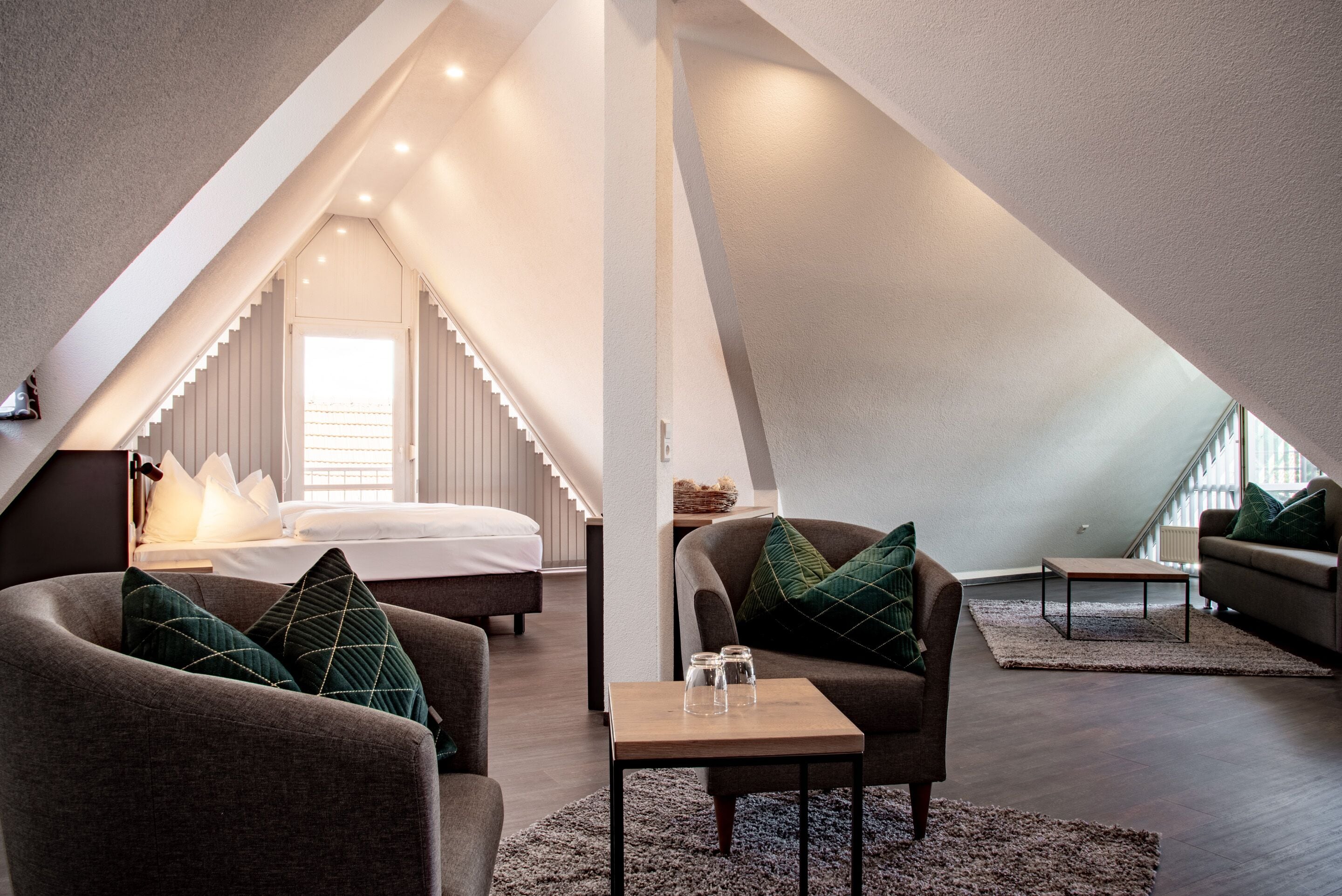 Een moderne loft slaapkamer met een schuine plafond, een groot bed, een zithoek met een bank en fauteuil, en een kleine tafel.