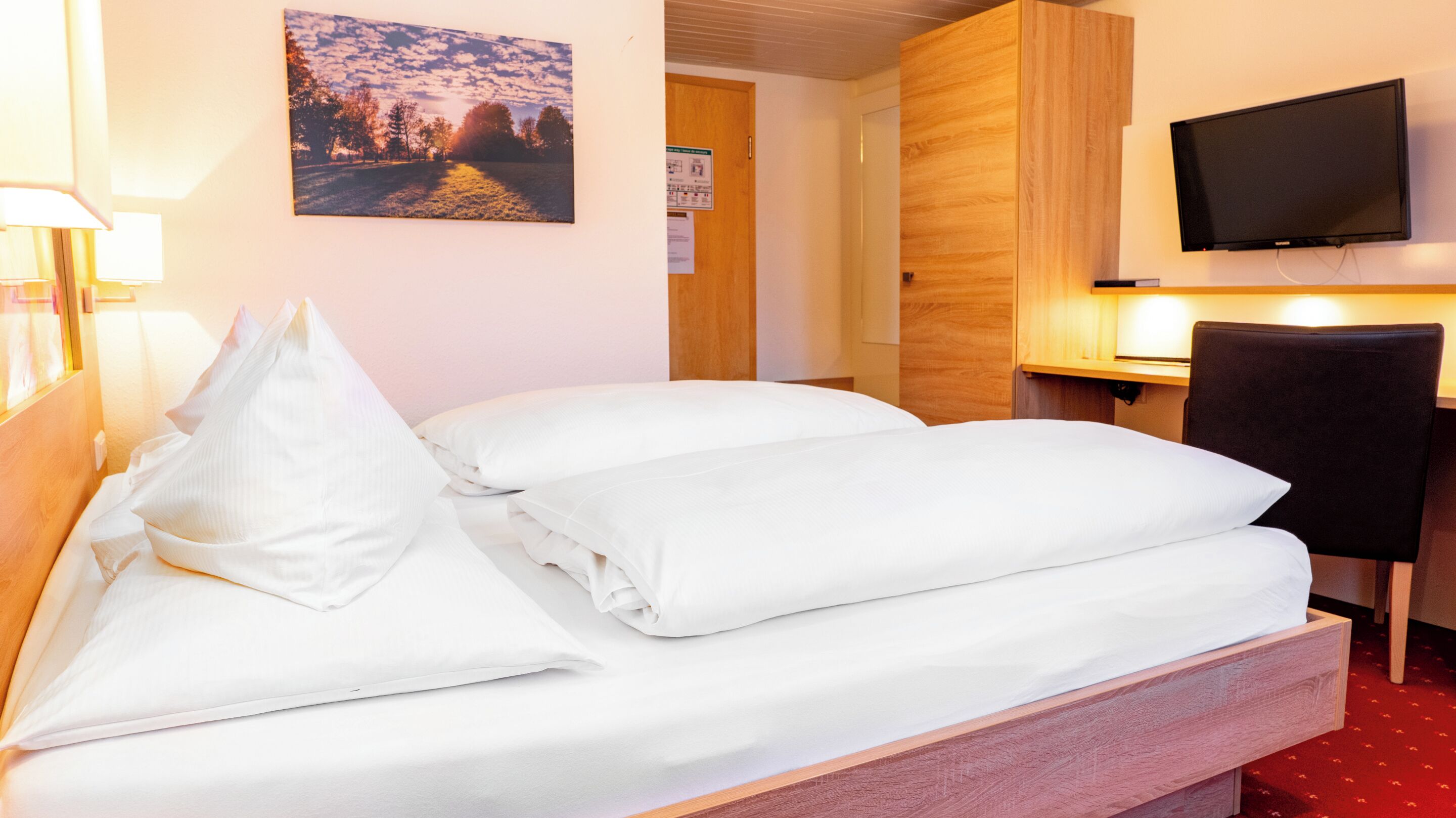 Habitación de hotel con cama, escritorio, silla, televisor y un cartel en la pared.