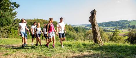 A group of people walking on a grassy path with a tree on the right and a view of a rural landscape in the background.