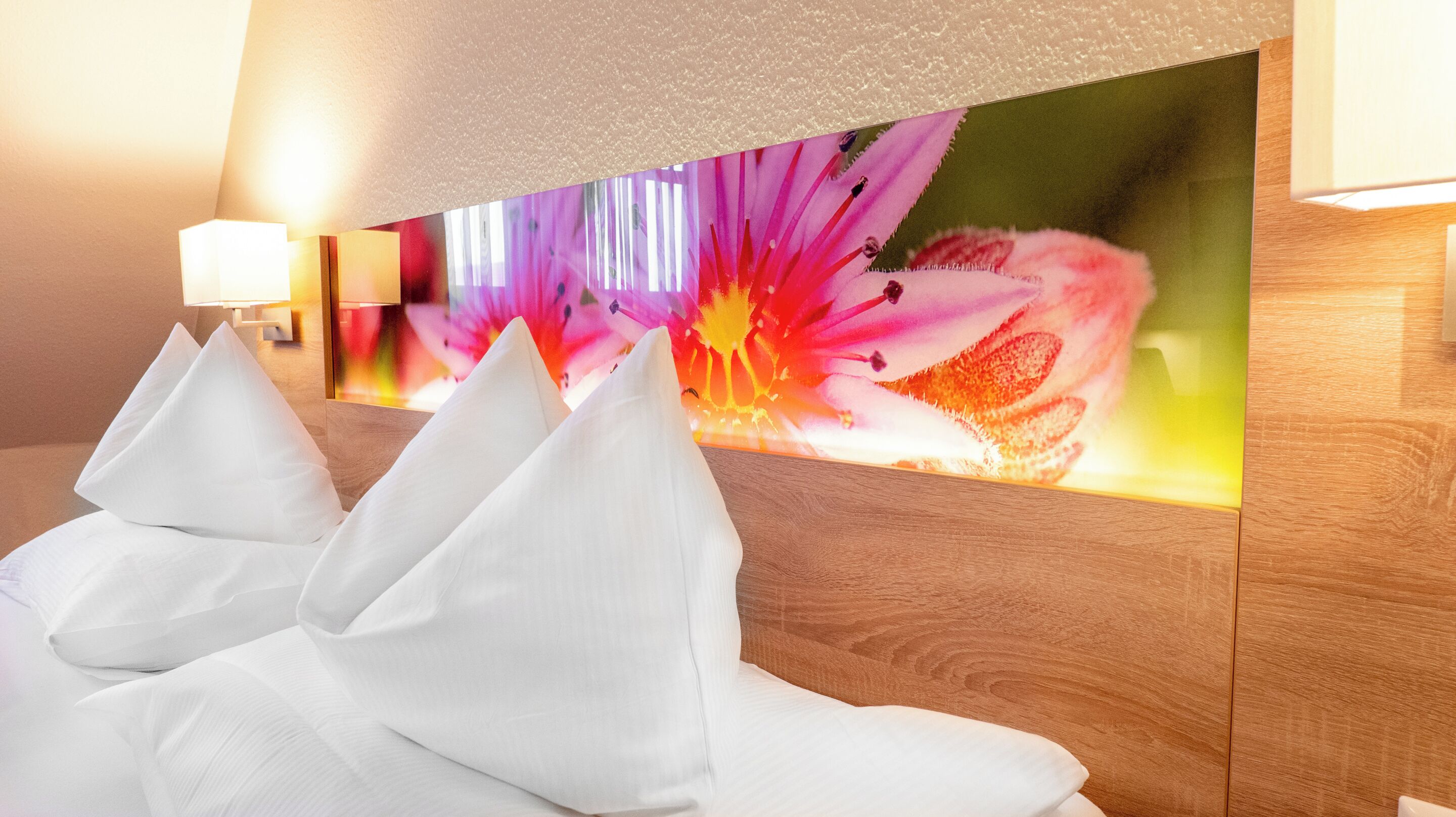 A hotel room with a wooden headboard, white pillows, and a large floral artwork on the wall.