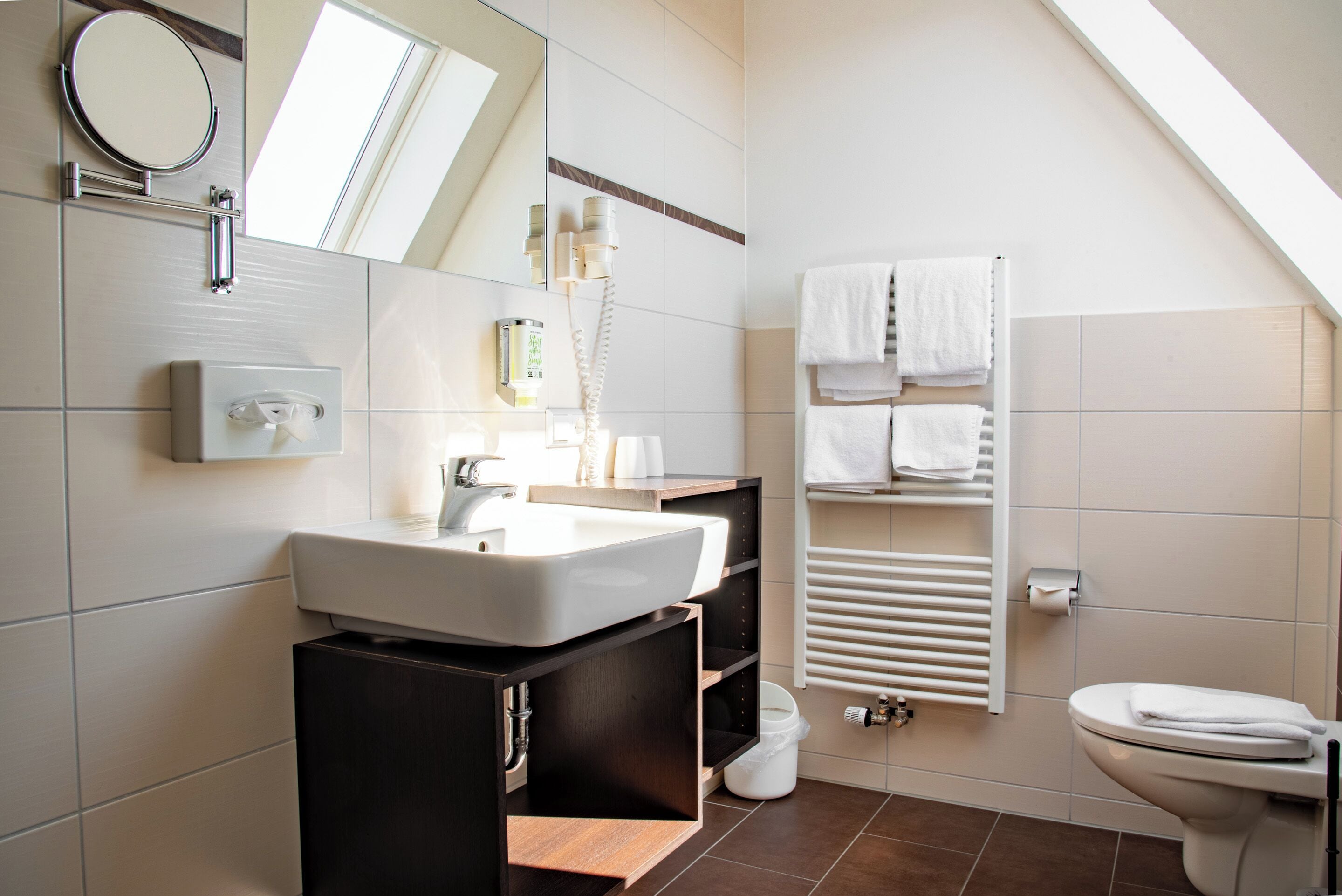 A modern bathroom with a large mirror, a sink, a towel rack, and a toilet.
