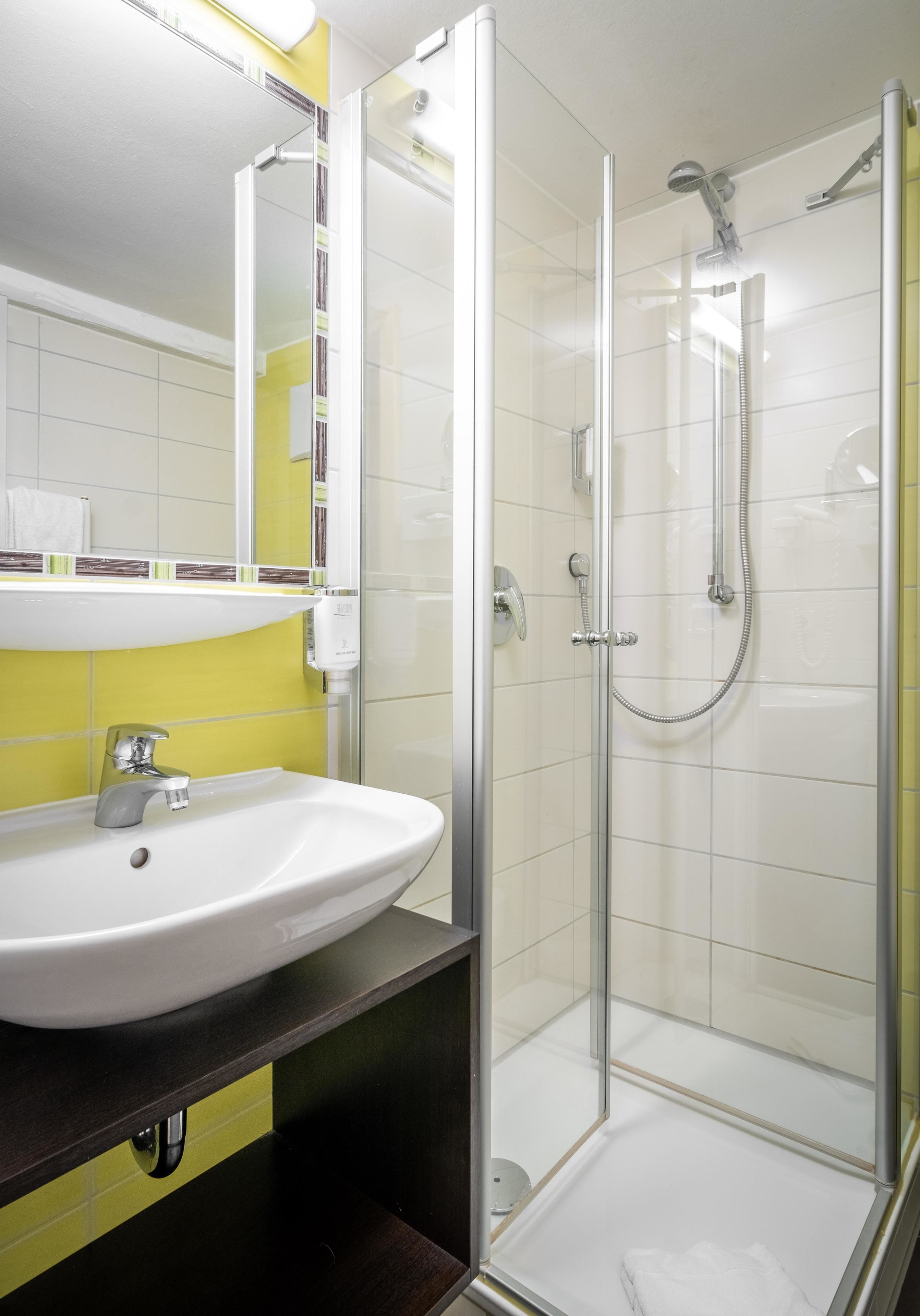 Un baño moderno con lavamanos blanco, tocador amarillo y negro, y mampara de ducha de vidrio.