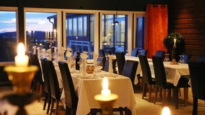 A restaurant with tables set for dining, candles on each table, and a view of the cityscape through large windows. - Hotell Silverhatten (Arjeplog)