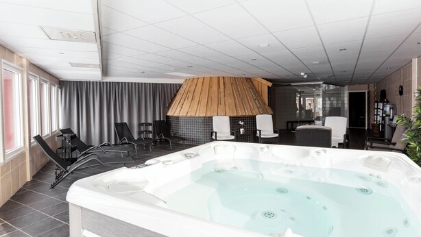 A modern spa area with a large hot tub, seating area, and a wooden structure. - Hotell Silverhatten (Arjeplog)