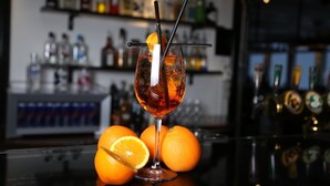 A cocktail glass with a straw and an orange slice on the rim, placed on a bar counter with oranges and a beer tap in the background. - Hotell Silverhatten (Arjeplog)