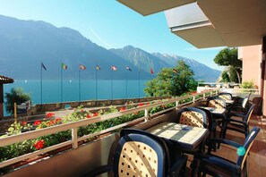 An outdoor terrace with tables and chairs, a view of a lake, and flags.