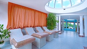 Un área de estar interior iluminada por el sol con sillones acolchados, un ventanal con cortinas anaranjadas y una planta en maceta.