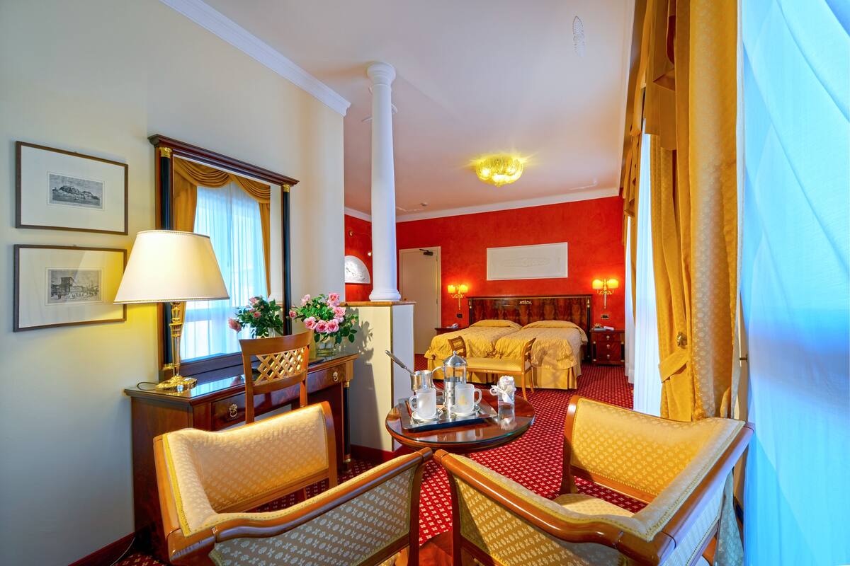 Quarto de hotel com uma cama, uma escrivaninha com abajur, duas cadeiras e uma pequena mesa com bandeja.