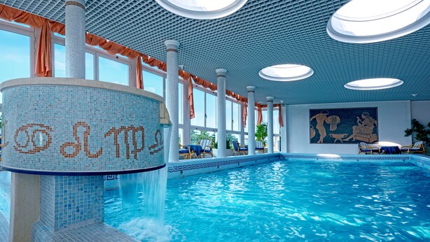 Una amplia piscina interior con agua cristalina azul, una pared de mosaicos y un techo con luces circulares.