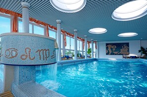 A large indoor swimming pool with clear blue water, a mosaic wall, and a ceiling with circular lights. - Hotel Aurora Terme (Abano Terme)