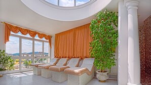 Una habitaci ón soleada con tres sillones de mimbre, una planta grande en maceta y vistas de la ciudad a través de amplias ventanas.