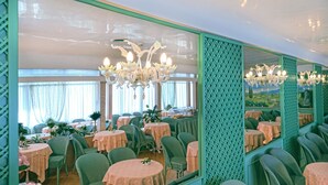 Un restaurante con mesas redondas, sillas verdes y un muro espejado que refleja el interior.