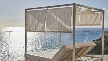A beachside outdoor seating area with a canopy, a single lounge chair, and a view of the ocean.