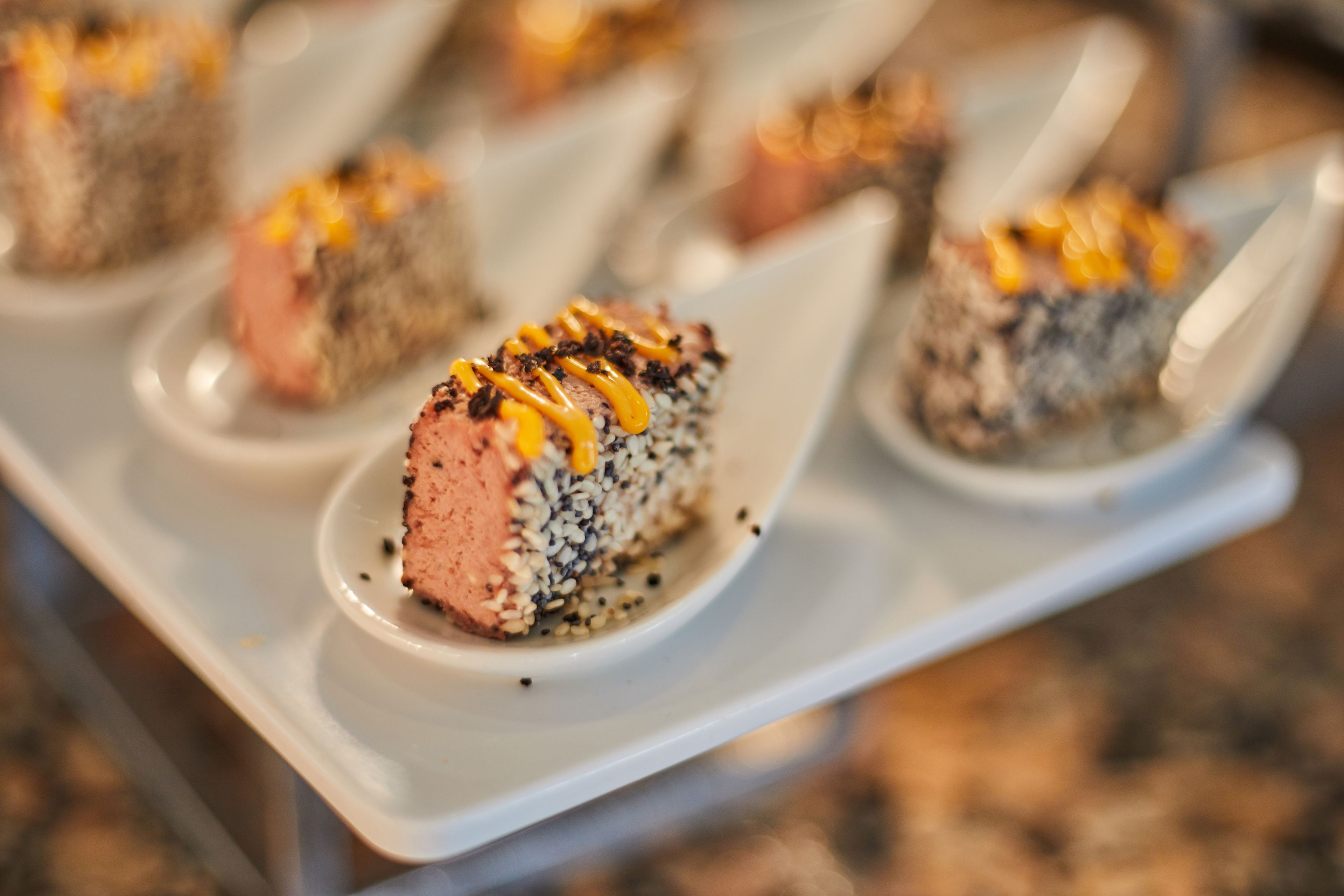A dessert tray with several pieces of cake topped with a yellow sauce and black seeds.