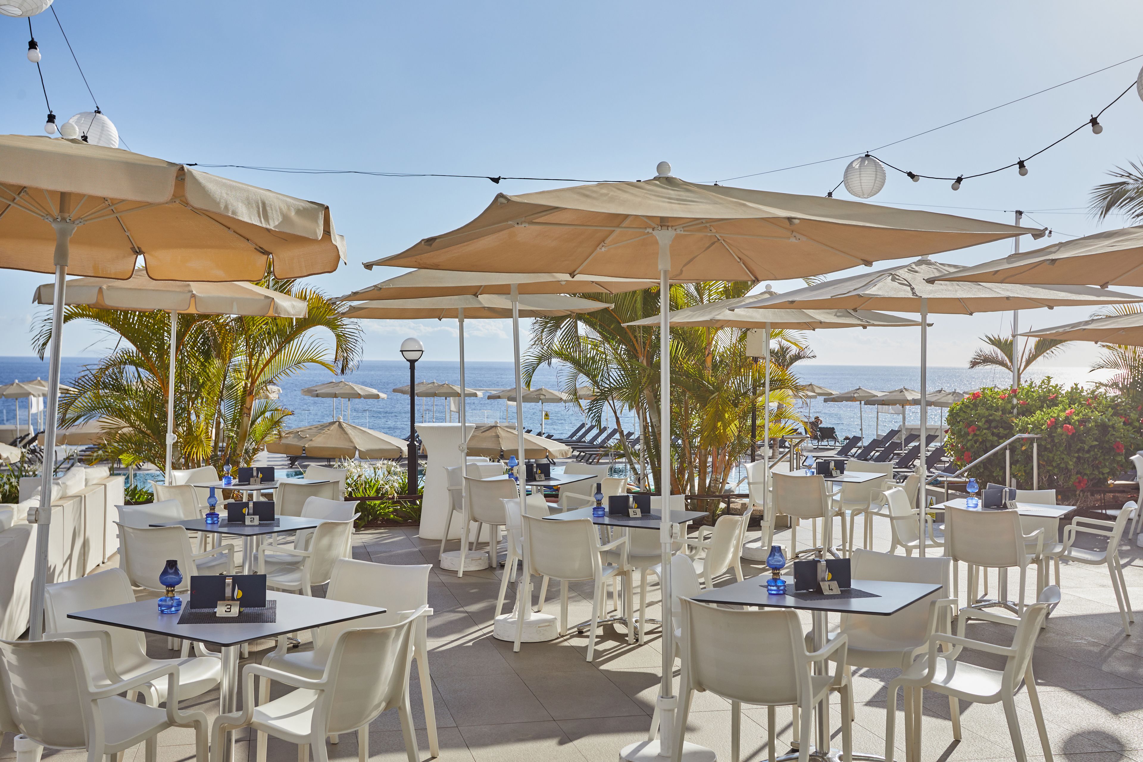 Un espace extérieur aménagé avec des tables et des chaises, protégé par de grands parasols et offrant une vue sur la plage.