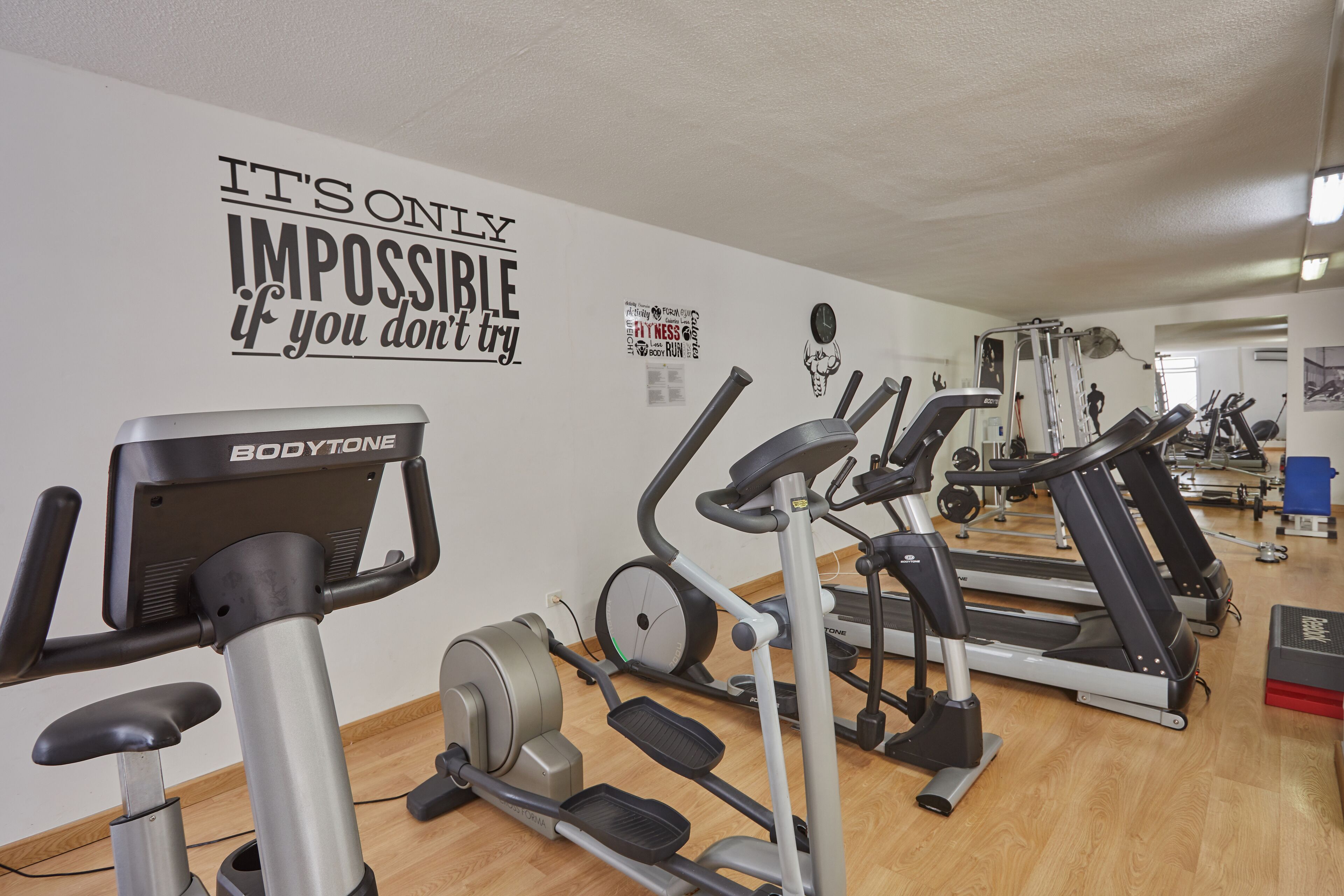 A gym with various exercise equipment, motivational wall art, and a wooden floor.