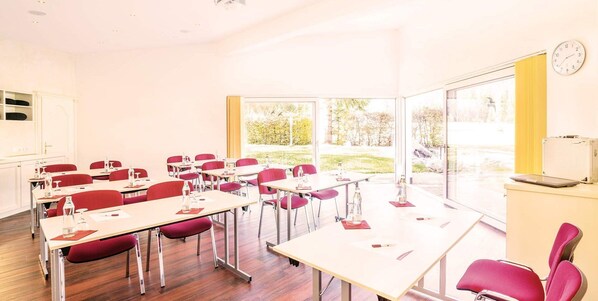 A conference room with tables and chairs, large windows, and a clock on the wall.