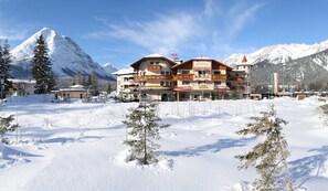 Een meerlaags hotel met een restaurant op de begane grond, omringd door met sneeuw bedekte bergen.