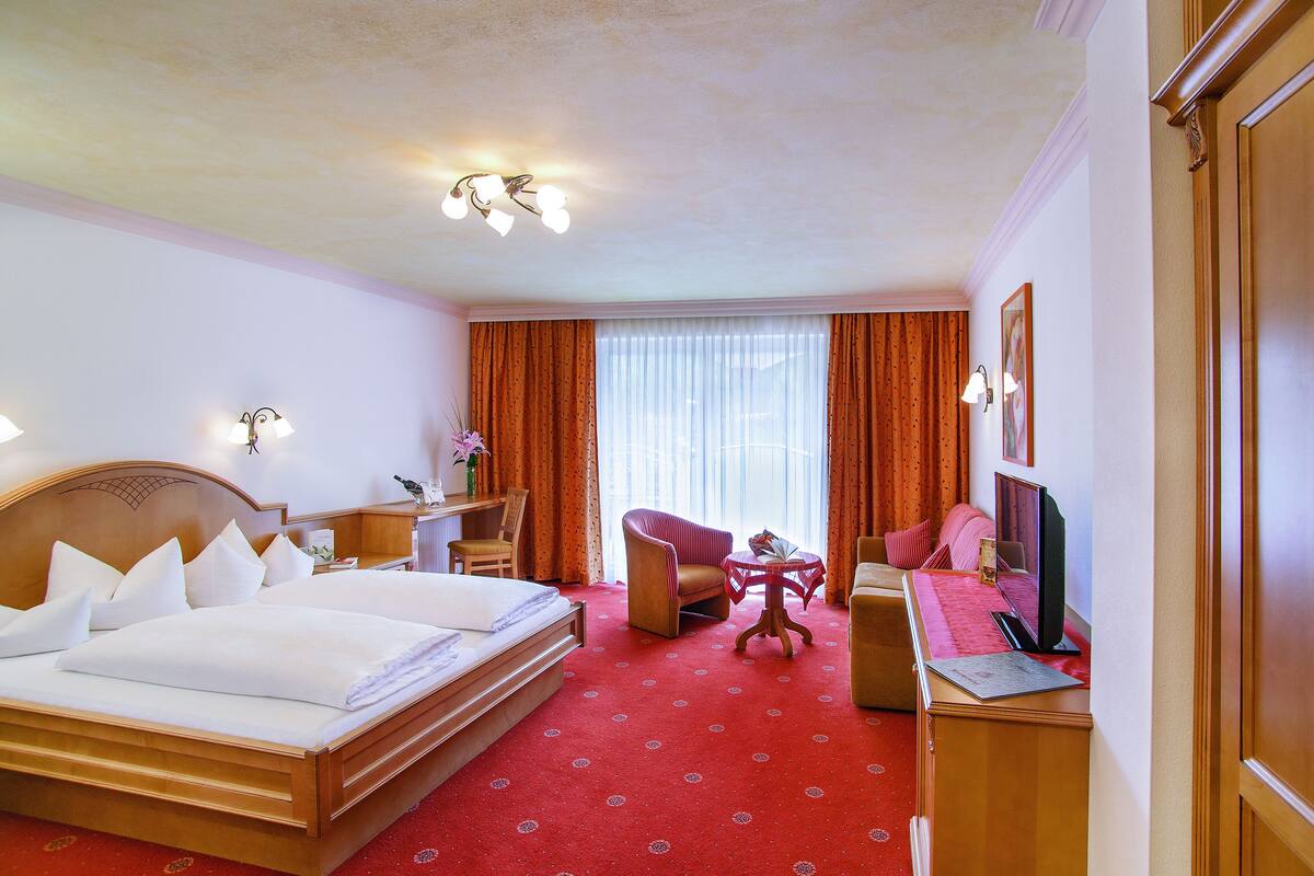 Ein Hotelzimmer mit einem großen Bett, einem Schreibtisch mit Computer, einem Sessel und einem Fernseher.