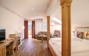 Een hotelkamer met een hemelbed van hout, een bureau met een computer, een bank en een televisie.