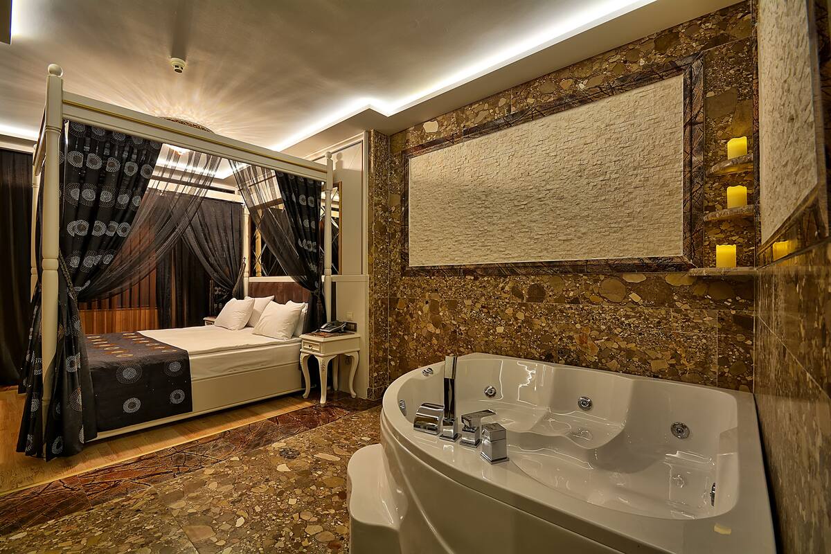 A bedroom with a four-poster bed, a large bathtub, and a stone wall.
