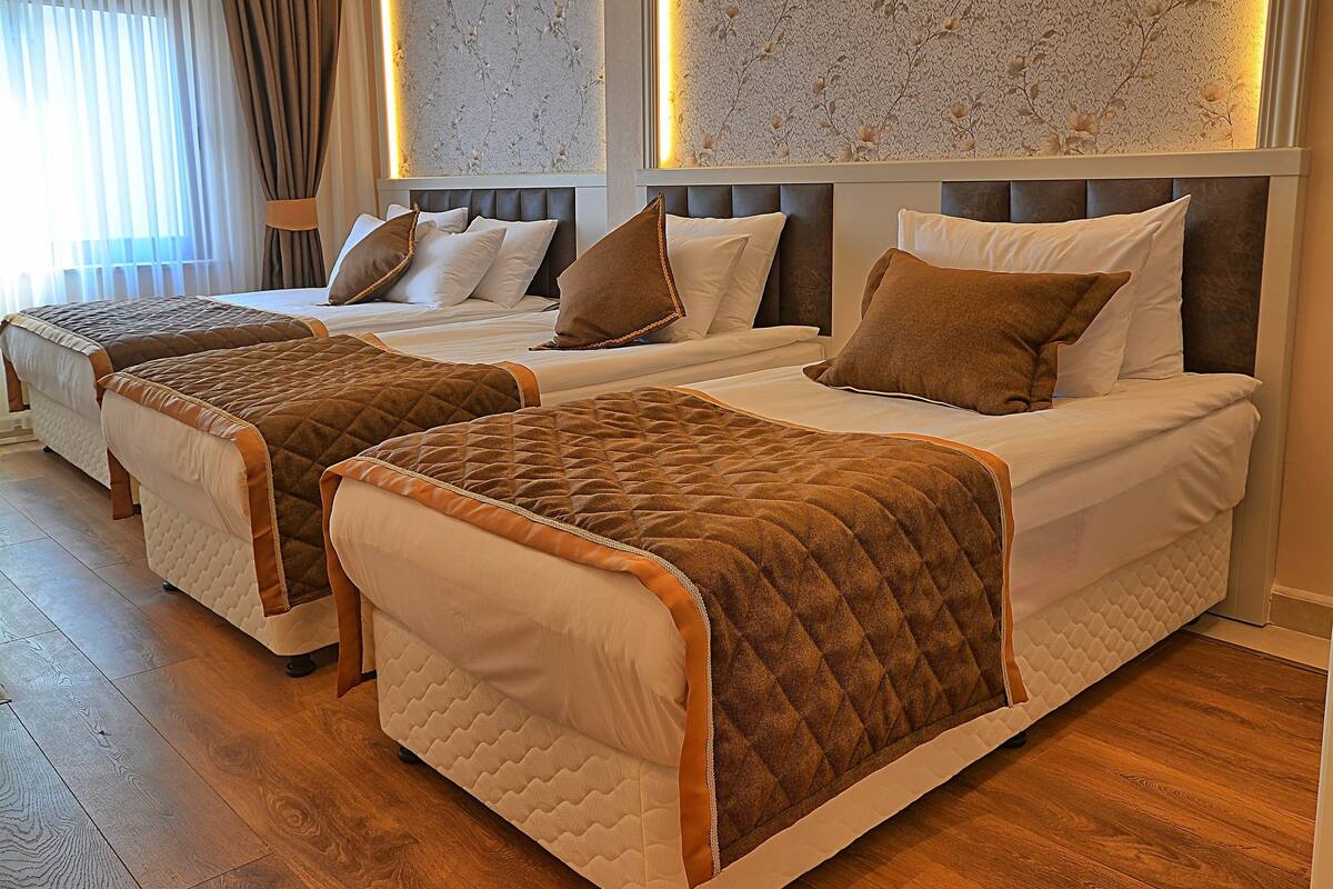 A hotel room with three beds, wooden flooring, and a patterned wallpaper.