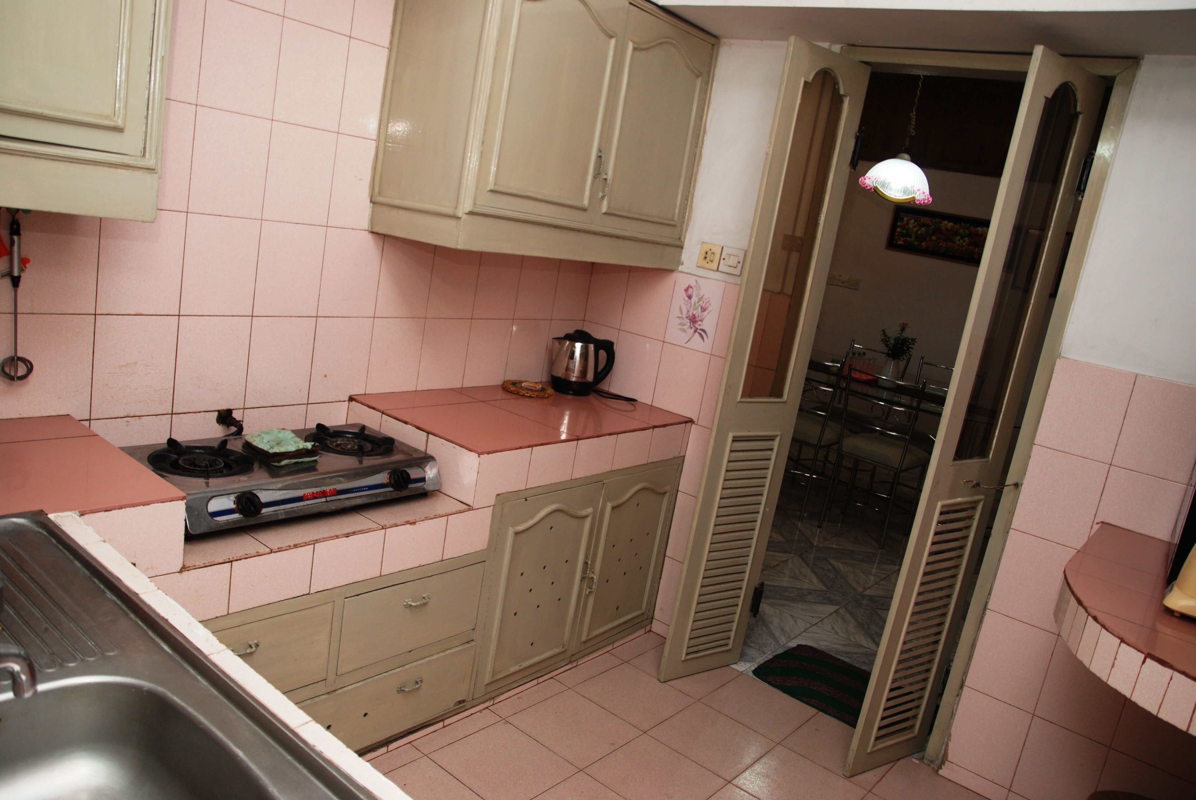 Een keuken met roze tegels, een gasfornuis, een spoelbak en kastjes.