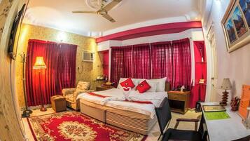 A bedroom with a large bed, red curtains, a ceiling fan, a desk, and a chair.