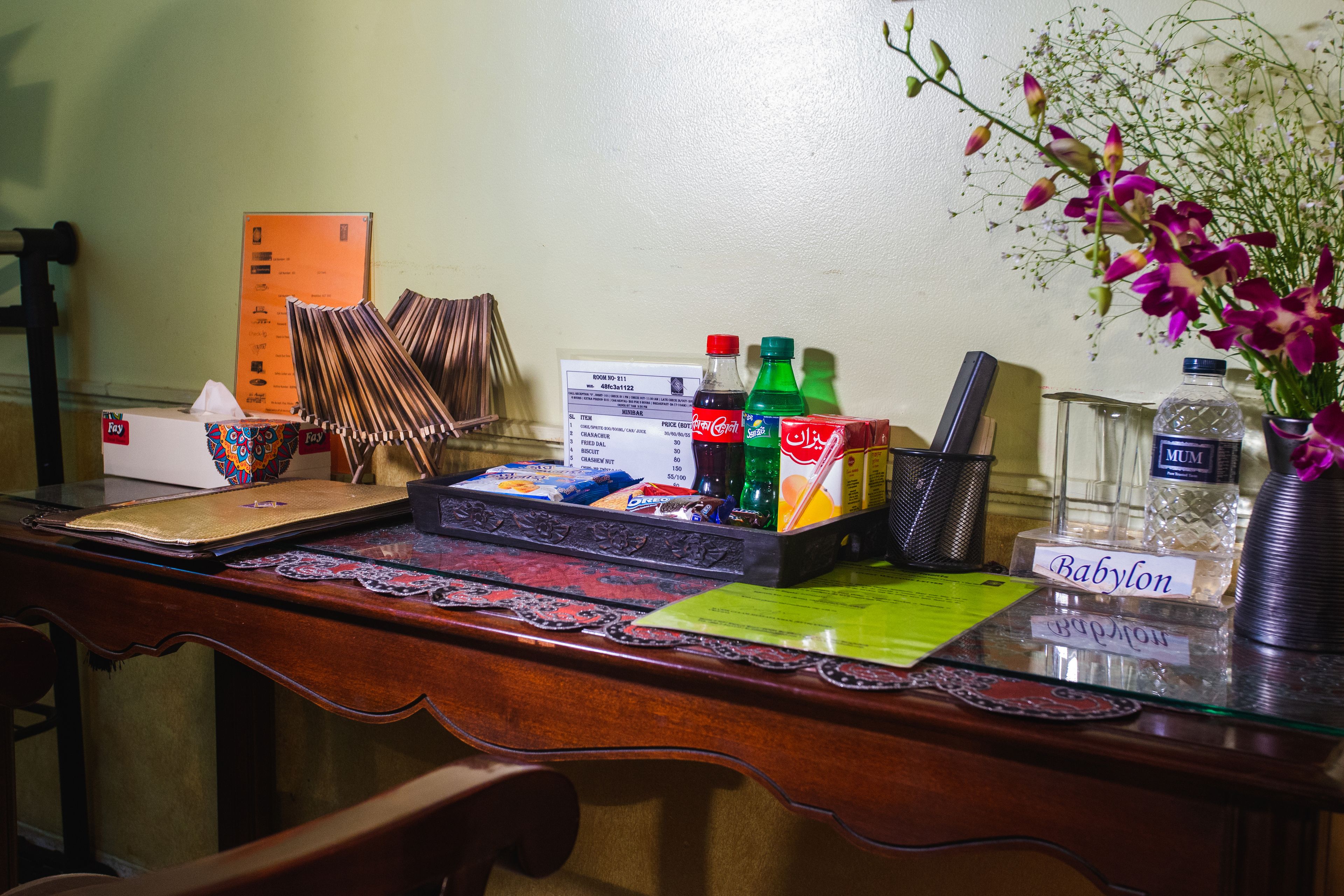 Een receptiebalie met een naambordje, een menubord en diverse spullen, zoals een zakdoekendoos, een Coca-Cola fles en een vaas met bloemen.