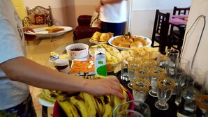 Ruokapöytä, jonka päällä on erilaisia ruokia ja juomia, kuten kulho täynnä hedelmiä, lautanen leivonnaisia ja useita lasillisia vettä.